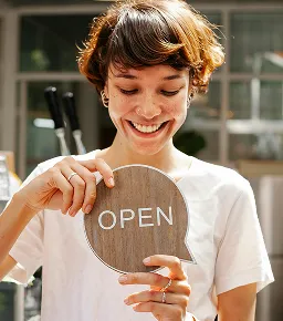 Woman holding an Open sign at a shop entrance